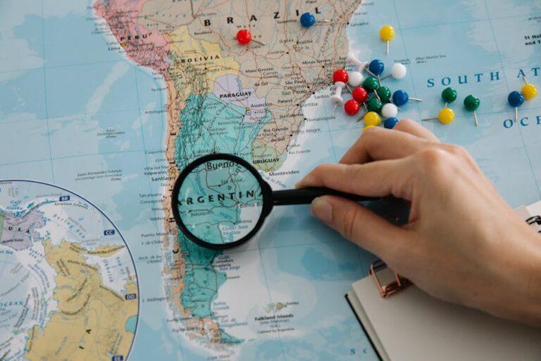 Close-up of a hand examining a South America map with a magnifying glass, highlighting Argentina.